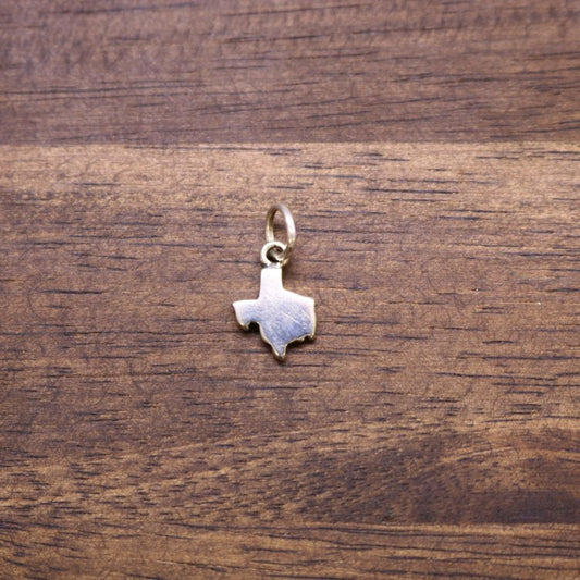 a gold texas state pendant on a wood surface